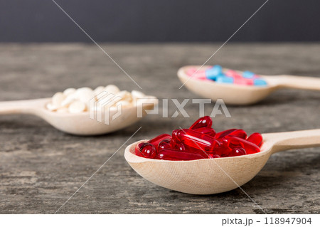 Vitamin capsules in a spoon on a colored background. Pills served as a healthy meal. Red soft gel vitamin supplement capsules on spoon 118947904