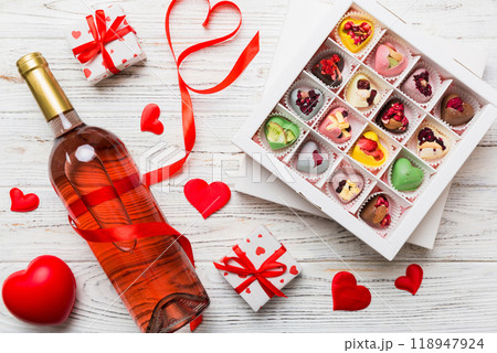 Bottle of red wine on colored background for Valentine Day with gift and chocolate. Heart shaped with gift box of chocolates top view with copy space Bottle of red wine on colored background for Valentine Day with gift and chocolate. Heart shaped with gift box of chocolates top view with copy space 118947924