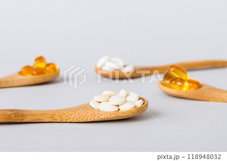 Vitamin capsules in a spoon on a colored background. Pills served as a healthy meal. Red soft gel vitamin supplement capsules on spoon Vitamin capsules in a spoon on a colored background. Pills served as a healthy meal. Red soft gel vitamin supplement capsules on spoon 118948032