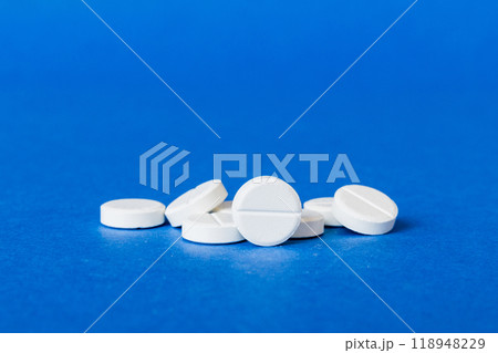 Heap of white pills on colored background. Tablets scattered on a table. Pile of red soft gelatin capsule. Vitamins and dietary supplements concept 118948229