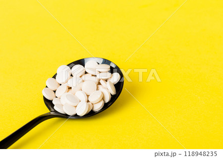 Heap of white pills on colored background. Tablets scattered on a table. Pile of red soft gelatin capsule. Vitamins and dietary supplements concept 118948235