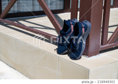 A pair of blue sneakers leaning against a brown column on the tiled floor, drying in the sun. 118948301