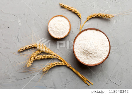 Flat lay of Wheat flour in wooden bowl with wheat spikelets on colored background. world wheat crisis Flat lay of Wheat flour in wooden bowl with wheat spikelets on colored background. world wheat crisis 118948342