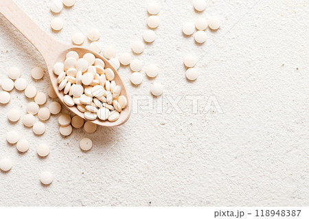 Heap of white pills on colored background. Tablets scattered on a table. Pile of red soft gelatin capsule. Vitamins and dietary supplements concept Heap of white pills on colored background. Tablets scattered on a table. Pile of red soft gelatin capsule. Vitamins and dietary supplements concept 118948387