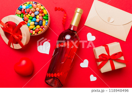 Bottle of red wine on colored background for Valentine Day with gift and chocolate. Heart shaped with gift box of chocolates top view with copy space 118948496