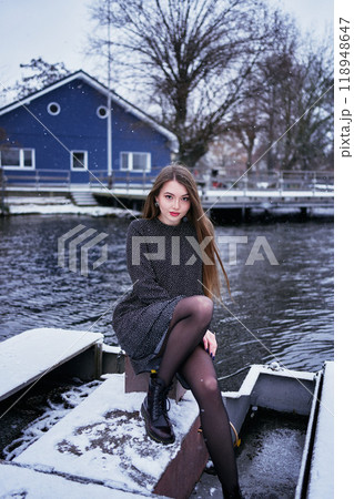 beautiful young woman with long blond hair in a light dress under the snowfall on the pier of the winter lake 118948647