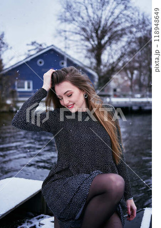 beautiful young woman with long blond hair in a light dress under the snowfall on the pier of the winter lake 118948649