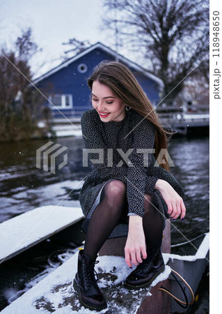beautiful young woman with long blond hair in a light dress under the snowfall on the pier of the winter lake beautiful young woman with long blond hair in a light dress under the snowfall on the pier of the winter lake 118948650