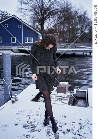 beautiful young woman with long blond hair in a light dress under the snowfall on the pier of the winter lake beautiful young woman with long blond hair in a light dress under the snowfall on the pier of the winter lake 118948659
