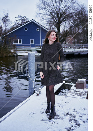 beautiful young woman with long blond hair in a light dress under the snowfall on the pier of the winter lake beautiful young woman with long blond hair in a light dress under the snowfall on the pier of the winter lake 118948660