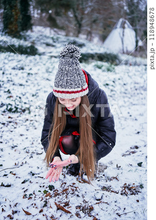 a beautiful young girl with long blond hair in a hat and a long down jacket plays with snow and enjoys winter nature a beautiful young girl with long blond hair in a hat and a long down jacket plays with snow and enjoys winter nature 118948678