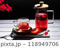Red fruit infusion in crystal glass and pitcher on white wooden table on dark background. 118949706