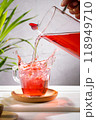 Pouring red fruit infusion and splashing from pitcher into glass on light background. Vertical format. 118949710