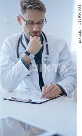 Doctor and a patient. The physician, wearing a white medical coat over a green shirt, gesturing with his hands during a consultation in the clinic. Medicine concept 118950031