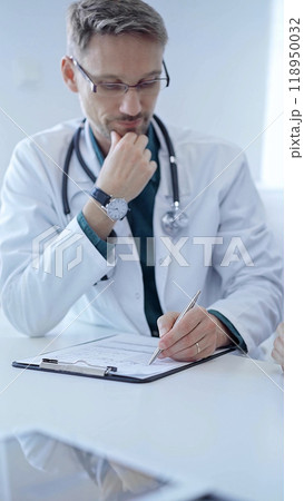 Doctor and a patient. The physician, wearing a white medical coat over a green shirt, gesturing with his hands during a consultation in the clinic. Medicine concept 118950032