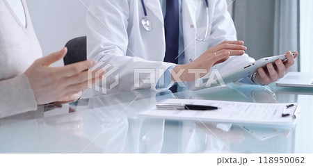 Doctor is consulting patient in modern clinic. Healthcare professional discusses medical information with a woman, using a tablet computer. Medicine concept 118950062