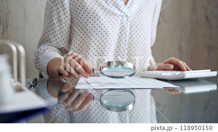 Auditor woman analyzing financial documents with magnifying glass and calculator at her office desk in formal white blouse with polka dots. Business people concept Auditor woman analyzing financial documents with magnifying glass and calculator at her office desk in formal white blouse with polka dots. Business people concept 118950150