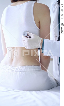 Doctor and patient. Physician wearing white medical gloves is using stethoscope examining woman lungs from the back side in clinic. Medicine and health care Doctor and patient. Physician wearing white medical gloves is using stethoscope examining woman lungs from the back side in clinic. Medicine and health care 118950171