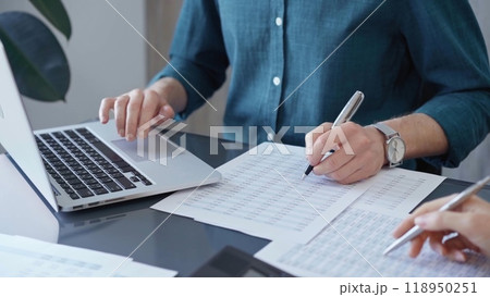 Business people professionals analyzing data on laptop. Close-up of auditor's hands reviewing financial spreadsheets in a modern office setting. Finance teamwork 118950251