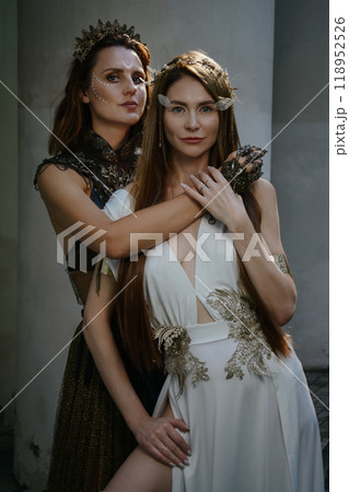 Two beautiful girls, sisters Lilith and Eva, pose in rocking dresses against the background of columns. Two beautiful girls, sisters Lilith and Eva, pose in rocking dresses against the background of columns. 118952526