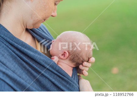 Mom walks with her newborn baby in a sling. This moment highlights the close bond between mother and child, promoting comfort, security, and the benefits of babywearing in everyday life 118952766