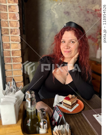 Millennial woman with red hair sits thoughtfully at a rustic cafe table, surrounded by a cozy and artistic atmosphere. Soft lighting and her pensive expression convey a sense of introspection and Millennial woman with red hair sits thoughtfully at a rustic cafe table, surrounded by a cozy and artistic atmosphere. Soft lighting and her pensive expression convey a sense of introspection and 118954526