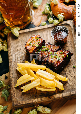 Close-up of barbecue ribs with crispy fries on a wooden board, served with a side of dipping sauce Close-up of barbecue ribs with crispy fries on a wooden board, served with a side of dipping sauce 118954612