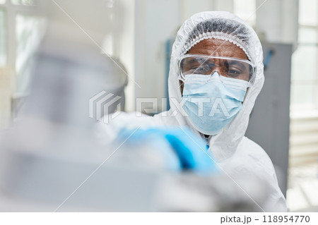 Close up of African American male production technician in protective mask and coveralls maintain factory equipment while working at pharmaceutical manufacturing plant, copy space Close up of African American male production technician in protective mask and coveralls maintain factory equipment while working at pharmaceutical manufacturing plant, copy space 118954770