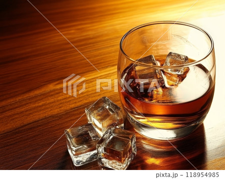 A glass filled with smooth single malt scotch whisky sits on a polished wooden table, ice cubes gently clinking against the glass, illuminated by warm, inviting light A glass filled with smooth single malt scotch whisky sits on a polished wooden table, ice cubes gently clinking against the glass, illuminated by warm, inviting light 118954985