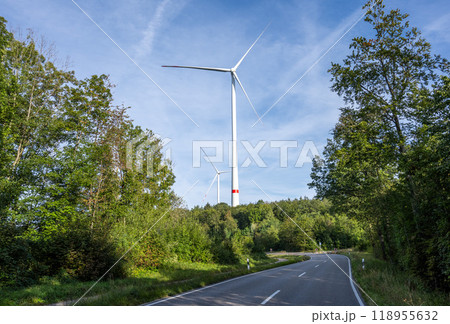 Winding asphalt road in the forest leading towards a wind farm Winding asphalt road in the forest leading towards a wind farm 118955632