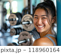 トレーニングジムでダンベルを持ち微笑む若い女性 118960164