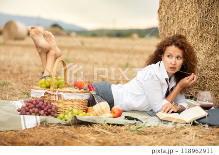 Woman in white blouse spends time in field, settled down in nature with book. 118962911
