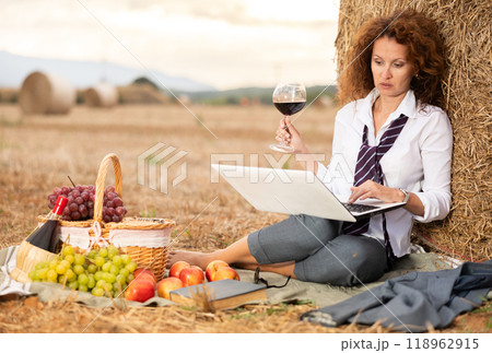 Woman spend time in field, settles down in nature with laptop and glass of wine Woman spend time in field, settles down in nature with laptop and glass of wine 118962915