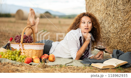 Woman in white blouse in office clothes, lying on blanket and reading book. Picnic on farm field Woman in white blouse in office clothes, lying on blanket and reading book. Picnic on farm field 118962935