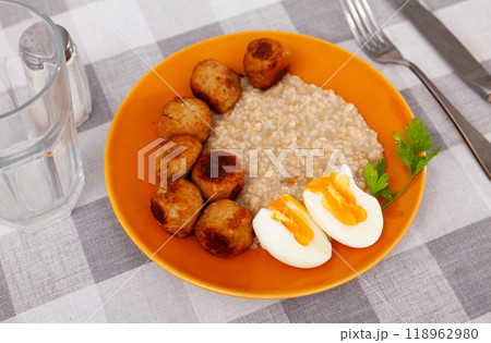 Homemade breakfast is served on plate - small portion of oatmeal, stewed meatballs and boiled egg Homemade breakfast is served on plate - small portion of oatmeal, stewed meatballs and boiled egg 118962980