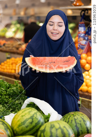 Delighted young Muslim woman purchaser choosing watermelon in grocery store 118963039