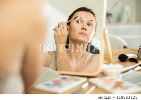 Woman applying eyebrow makeup with brush in front of mirror 118963128