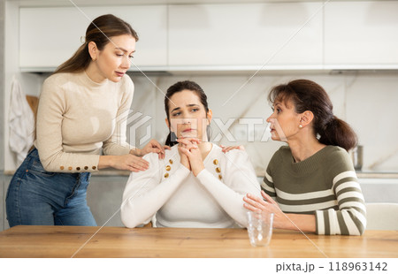 Sad middle-aged woman sitting at table while two others trying to calm her 118963142