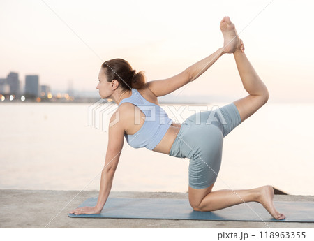 Positive sporty skilled young female teacher demonstrating table pose of yoga on seashore at sunrise Positive sporty skilled young female teacher demonstrating table pose of yoga on seashore at sunrise 118963355