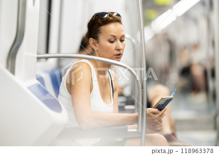 Adult woman sitting in subway car with phone 118963378