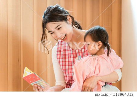 保育園・幼稚園・託児所・保育所で園児の女の子に絵本を読み聞かせする女性保育士・保母さん・シッター 118964312