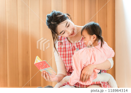 保育園・幼稚園・託児所・保育所で園児の女の子に絵本を読み聞かせする女性保育士・保母さん・シッター 保育園・幼稚園・託児所・保育所で園児の女の子に絵本を読み聞かせする女性保育士・保母さん・シッター 118964314