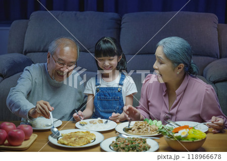 Happy Asian family grandparent and granddaughter dining on table and having fun during at house evening time, Happiness senior parent and child eating dinner food together in living room indoors 118966678