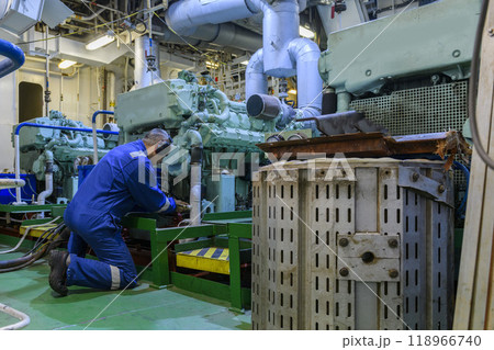 Marine Engineer in blue overall working in Engine room of ship. Work at sea. Motorman. 118966740