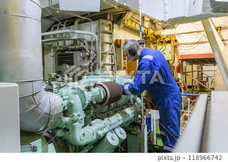 Marine Engineer in blue overall working in Engine room of ship. Work at sea. Motorman. 118966742