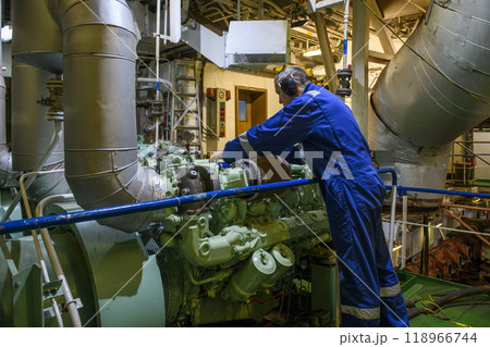 Marine Engineer in blue overall working in Engine room of ship. Work at sea. Motorman. 118966744