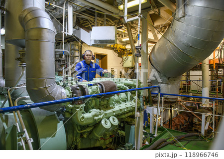 Marine Engineer in blue overall working in Engine room of ship. Work at sea. Motorman. 118966746