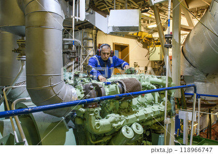 Marine Engineer in blue overall working in Engine room of ship. Work at sea. Motorman. 118966747
