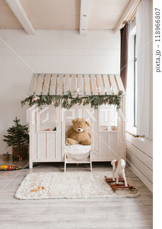Teddy bear is sitting in a wooden playhouse with a Christmas tree in the background 118966807
