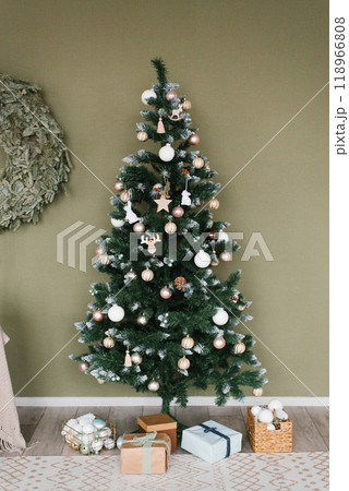 Large Christmas tree with many ornaments on it is surrounded by boxes and a wreath 118966808